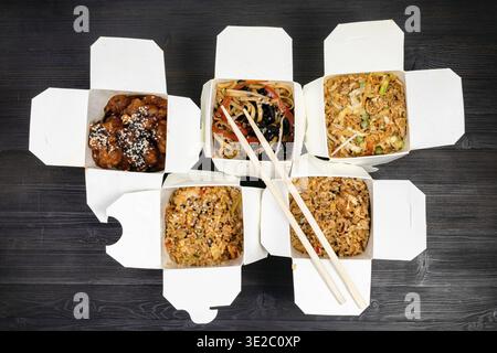 Top view of chinese fast food in disposable cardboard boxes and wooden chopsticks on black table Stock Photo
