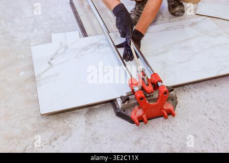 Worker cuts large tiles for flooring using manual tile cutter in home renovation project. Stock Photo