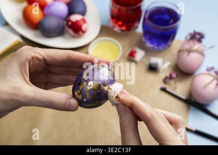 Happy Easter! Close-up of woman's hands painting an easter egg. Decorating Easter eggs with gold leaf. Step by step instructions. DIY concept. Step 5 Stock Photo