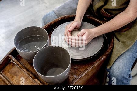 Woman working on the potter's wheel. Ceramist young woman making clay product on pottery lathe in studio. Close up of female hands working on potters Stock Photo