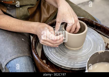 Woman working on the potter's wheel. Ceramist young woman making clay product on pottery lathe in studio. Close up of female hands working on potters Stock Photo