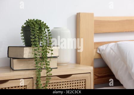 Books and potted houseplant on nightstand near bed indoors, closeup Stock Photo