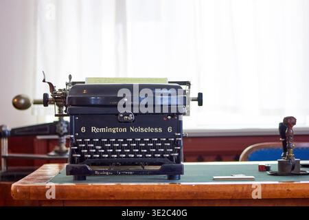 A vintage black Remington Noiseless 6 typewriter sits prominently centered on a wooden desk with a green felt writing pad. The antique mechanical... Stock Photo