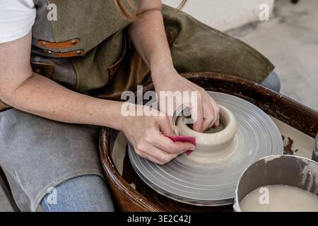 Woman working on the potter's wheel. Ceramist young woman making clay product on pottery lathe in studio. Close up of female hands working on potters Stock Photo