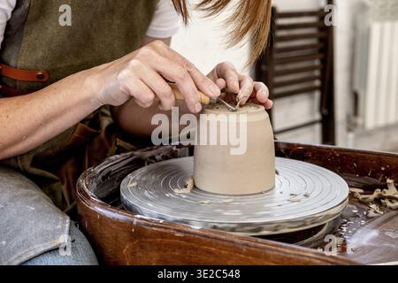 Woman working on the potter's wheel. Ceramist young woman making clay product on pottery lathe in studio. Close up of female hands working on potters Stock Photo