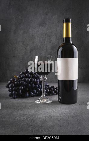 Glass and bottle of red wine with grapes on dark background. Red wine with cheese and fruits. Wine bottle mockup with blank labels to place your desig Stock Photo