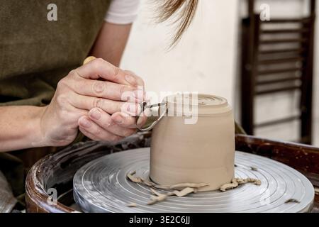 Woman working on the potter's wheel. Ceramist young woman making clay product on pottery lathe in studio. Close up of female hands working on potters Stock Photo