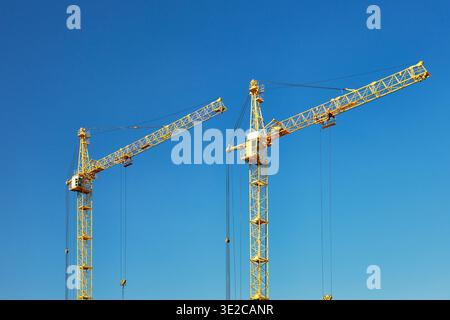 Two tall construction tower cranes against a blue sky. Stock Photo