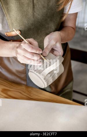 Close up female hands make dishes from clay. Woman potter in apron making pottery in studio Stock Photo