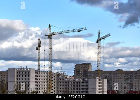 Three tall construction tower cranes are working on the construction of a multi-story apartment building in the city. Stock Photo