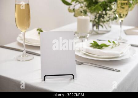 Mockup white blank space card for table number or menu. Wedding teble decoration with white flowers, glasses and white napkins. Elegantly decorated ta Stock Photo