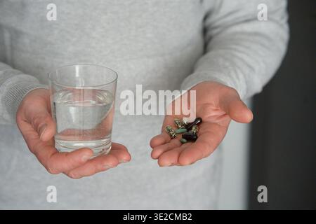 A man holds a glass of water and a handful of various tablets and capsules. High quality photo Stock Photo