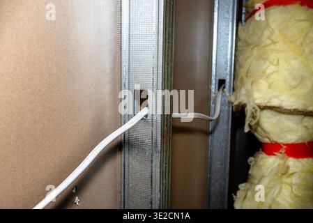 Builders installing metal studs, electrical cables, and insulation during interior construction Stock Photo