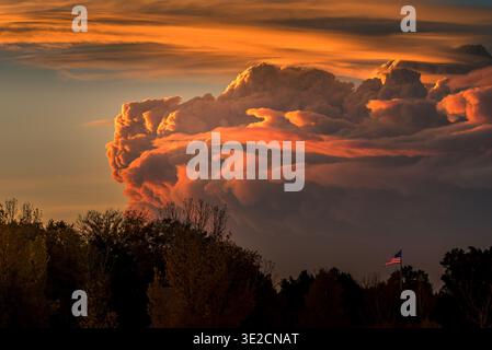 Dramatic Orange Cumulonimbus Sunset Over Trees With American Flag on Flagpole at Dusk Stock Photo
