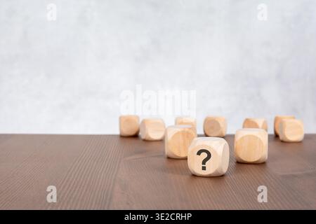 Low angle close-up of a wooden toy block with a black question mark printed on it. The foreground block is in sharp focus, while a group of empty wood Stock Photo