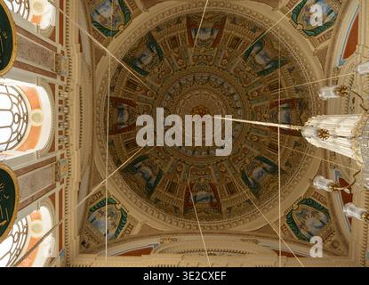 Low angle view of an ornate gilded mosque dome ceiling with detailed Islamic geometric patterns painted panels and crystal chandelier creating a grand Stock Photo
