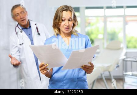 Upset female doctor with papers stading in office with disgruntled chief Stock Photo