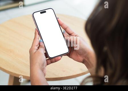 Hands holding mobile phone mockup with white screen over wooden table for remote work and productivity concept Stock Photo