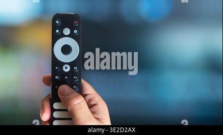Hand using a modern TV remote control with copy space on a TV background, smart home technology concept Stock Photo