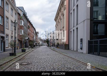 Quiet empty cobblestone street lined with historic facades modern buildings and street lamps in a European city center under an overcast sky with stro Stock Photo