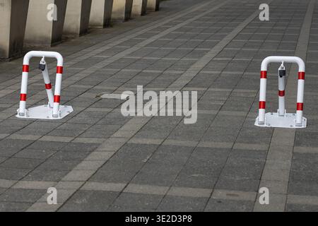 Two white and red bollards with integrated locks standing on a grey cobblestone sidewalk, defining a secured parking area or restricted access zone Stock Photo