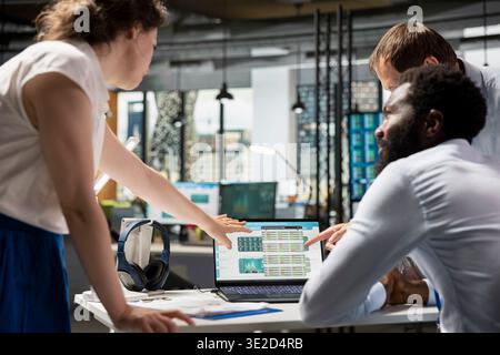 Black man and two caucasian colleagues analyzing charts, graphs and financial data on laptop. Business analysts collaborating on investment strategies and company reports in office. Stock Photo