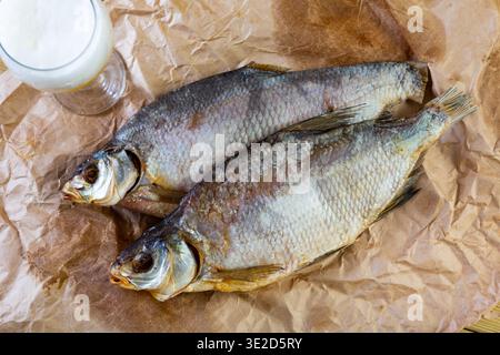 On table covered with paper is beer and snack - dried jerked bream, whole fish Stock Photo