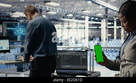 Engineer using isolated screen smartphone in server room while optimizing deep learning systems handling tasks. Data center worker uses chroma key mobile phone, adjusting AI model parameters, camera A Stock Photo