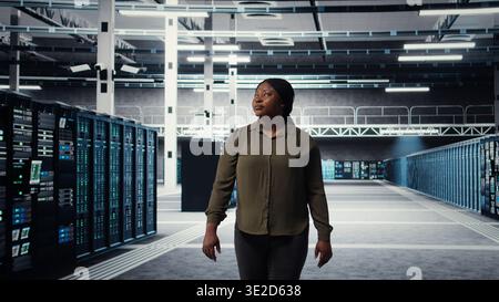 Portrait of smiling data center admin conducting security audit to protect against cyber threats. Happy supervisor walking in server room, pleased by compliance with industry standards, camera A Stock Photo