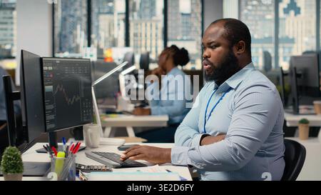 Portfolio manager in prop firm office analyzes stock market trends to enhance investment returns. African american man tracks performance metrics to identify investment opportunities Stock Photo