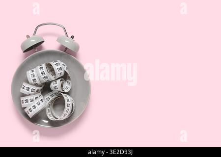 Alarm clock made of plate with tape measure on pink background. Intermittent fasting concept Stock Photo