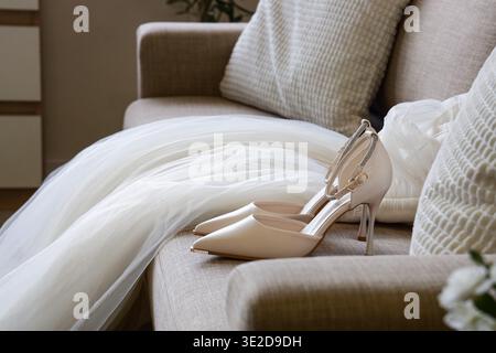 Stylish high heels with wedding dress on sofa in living room Stock Photo