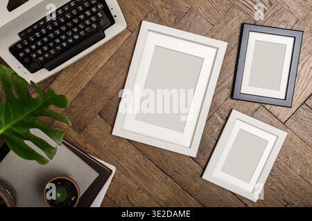 Three blank photo frames in different sizes on herringbone wood floor. Vintage typewriter, monstera plant and cactus. Art print and poster mockup. Vin Stock Photo