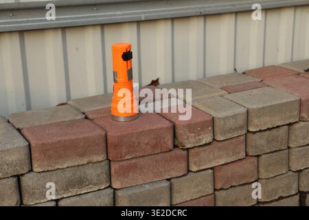 A bright orange flashlight stands on a row of stacked concrete bricks. The scene shows a simple arrangement of building materials under natural light. Stock Photo