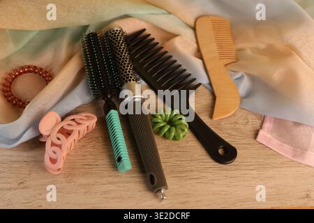 Various hair styling tools and accessories are placed on a wooden surface. The scene includes brushes, a comb, hair ties, and fabric in soft colors. Stock Photo