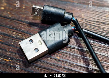 Frayed black USB and micro USB charging cable, insulation torn to reveal colorful internal wires. Symbolizes electronic device failure and wear Stock Photo