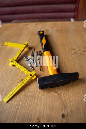 A simple arrangement of essential construction tools: hammer, nails, and a yellow folding rule on wood. Stock Photo
