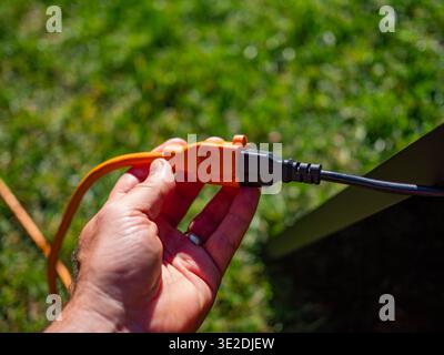 Hand holding an orange outdoor extension cord as it plugs into a black power cable Stock Photo