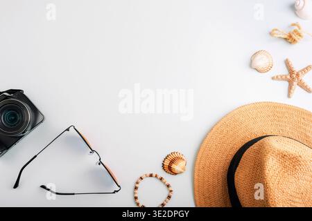 Summer beach accessories with straw hat, camera, sunglasses, bracelet and seashells on light blue background. Top view, flat lay, copy space. Travel c Stock Photo