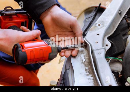Technician worker uses power screwdriver tool to install car part in garage Stock Photo