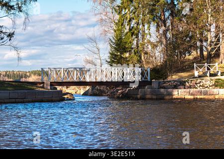 Wooden bridge with white railings connecting the two banks across a small channel in the city park on a sunny spring day. Stock Photo
