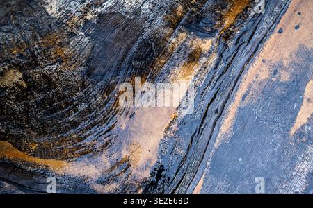 Abstract weathered stone surface reveals ancient, textured patterns. Deep cracks split earthy tones, streaked with gold and gray. Stock Photo