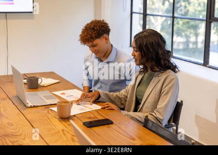 African American colleagues sitting in meeting room reviewing charts with laptop and smartphone Stock Photo