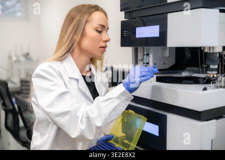 Laboratory technician inserting HPLC vials into advanced analytical equipment for testing in a pharmaceutical lab. Stock Photo