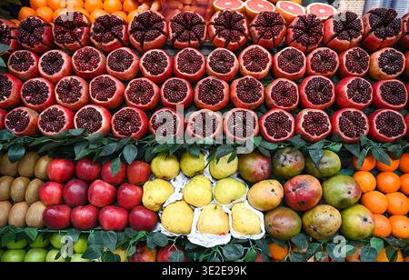 Rows of vibrant, sliced pomegranates, red apples, yellow pears, green kiwis, and colorful oranges are attractively displayed on a market stall Stock Photo