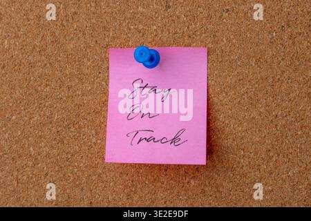 A note with handwritten text Stay On Track is pinned to a corkboard. Motivation, business planning, productivity, and goal setting concept. Stock Photo