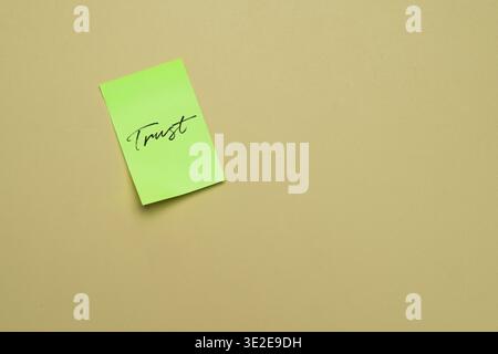 A green sticky note with the handwritten word trust in the upper left on a neutral beige background. Business ethics, integrity, and reliability Stock Photo