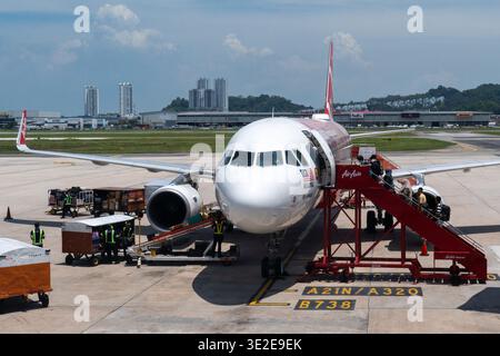 A front view of an AirAsia Airbus A320 aircraft at an airport gate. Passengers are boarding via a mobile staircase Stock Photo