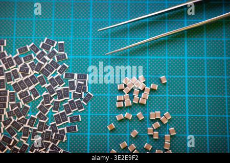 SMD resistors and capacitors with tweezers on cutting mat, electronics assembly concept Stock Photo