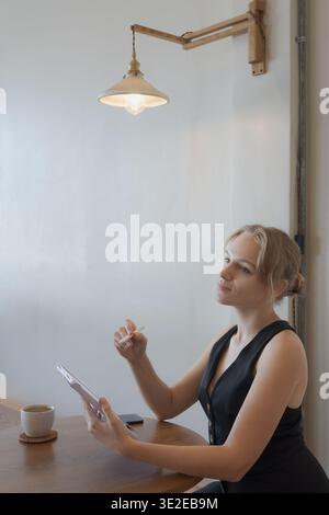Casual young business woman using digital tablet while sitting at table in cafe Stock Photo
